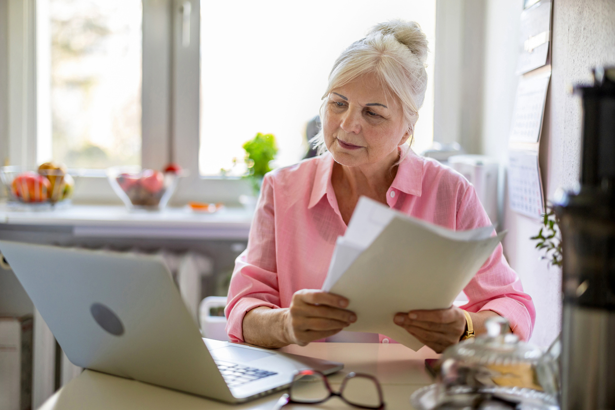 Image of a woman holding papers and looking at a laptop.