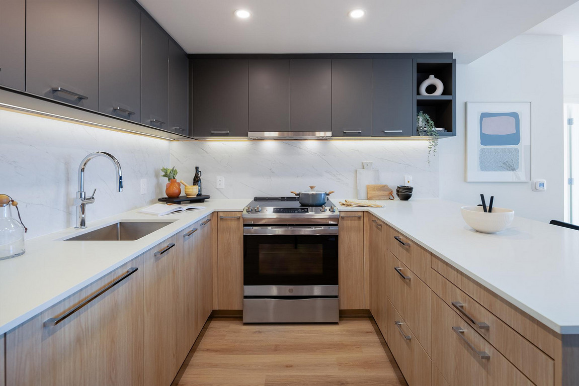 Victor_Kitchen_Close-up Bright kitchen with dark grey upper cabinets, quartz backsplash with natural veining, white countertop, wood-grain lower cabinets and flooring, and modern appliances.