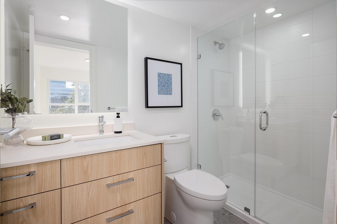 Victor_Bathroom Clean white bathroom with glass shower, large mirror, and wood-grain vanity with drawers