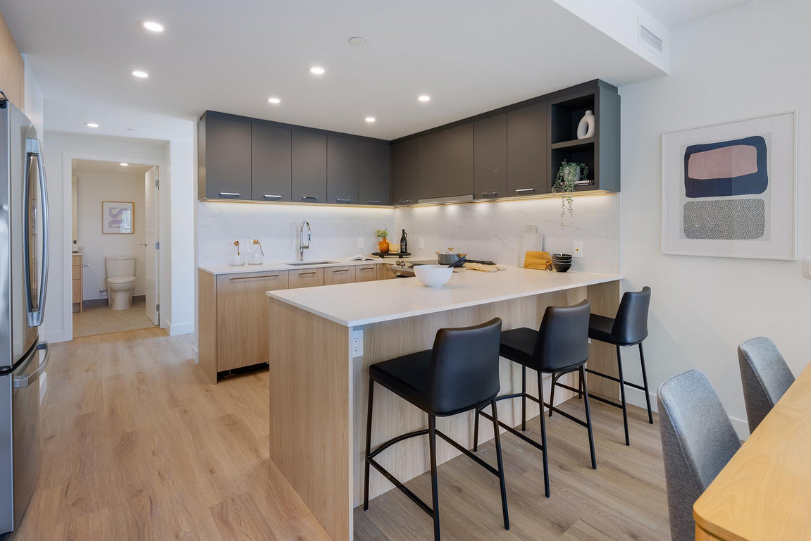 Victor_Kitchen Contemporary u-shaped kitchen with two-tone wood and grey cabinetry, white countertop, modern appliances and black stools