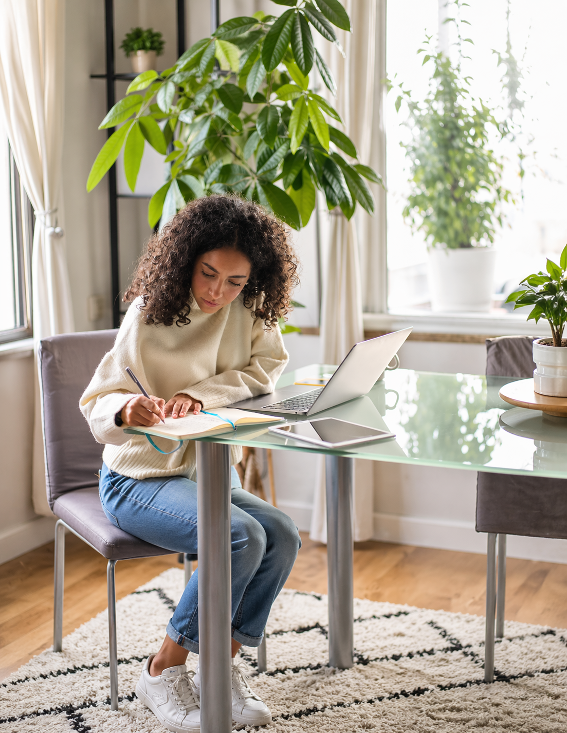 Person writing while working on a laptop at a table