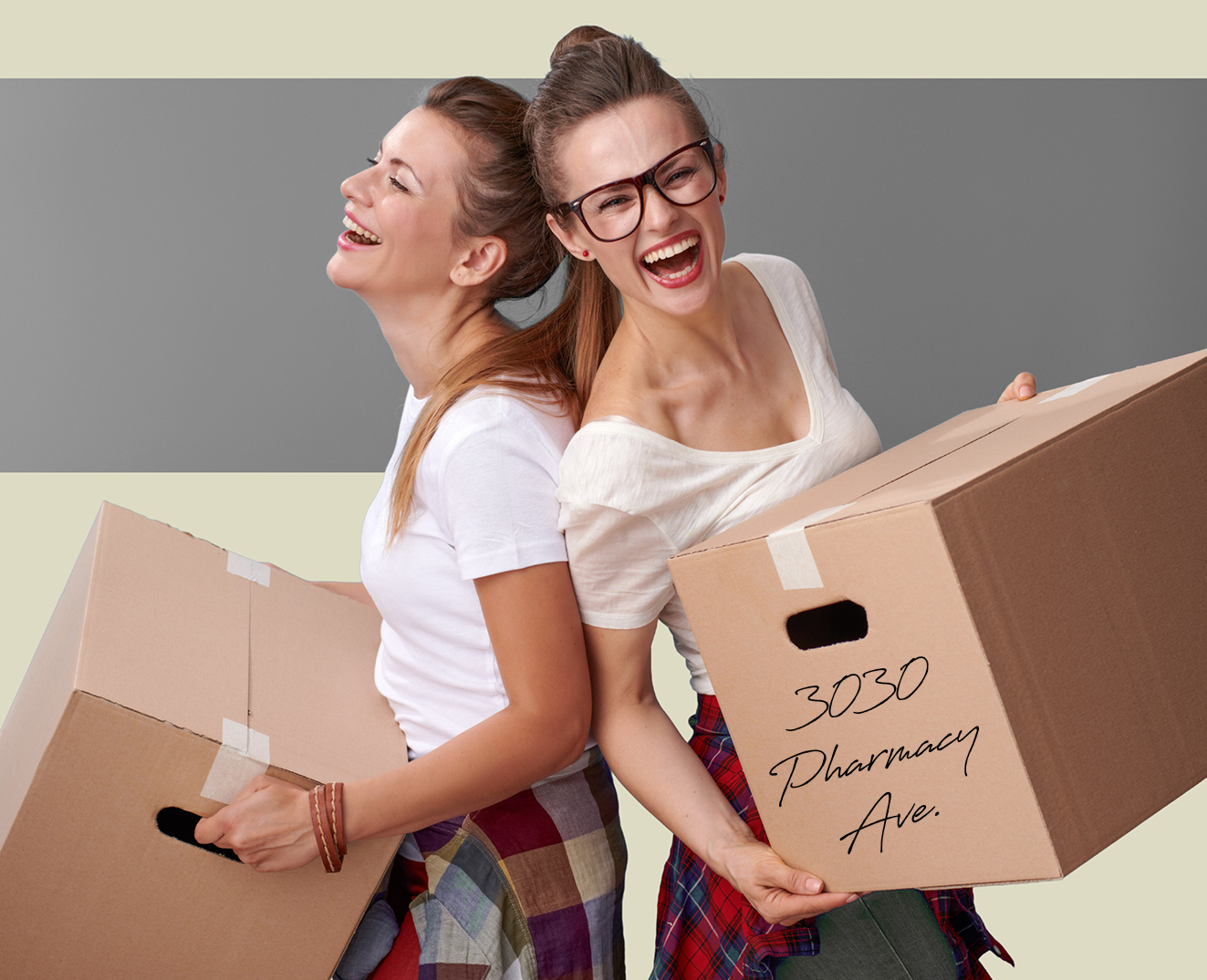 Two women laughing back-to-back while carrying moving boxes labelled 
