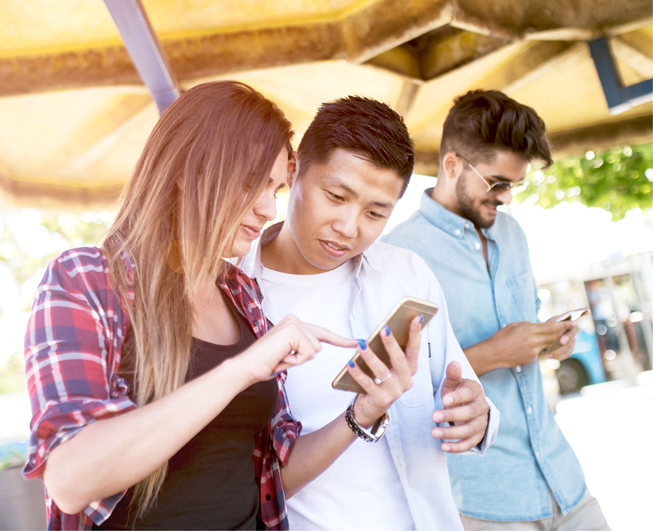 Friends looking at a smartphone together outdoors on a sunny day
