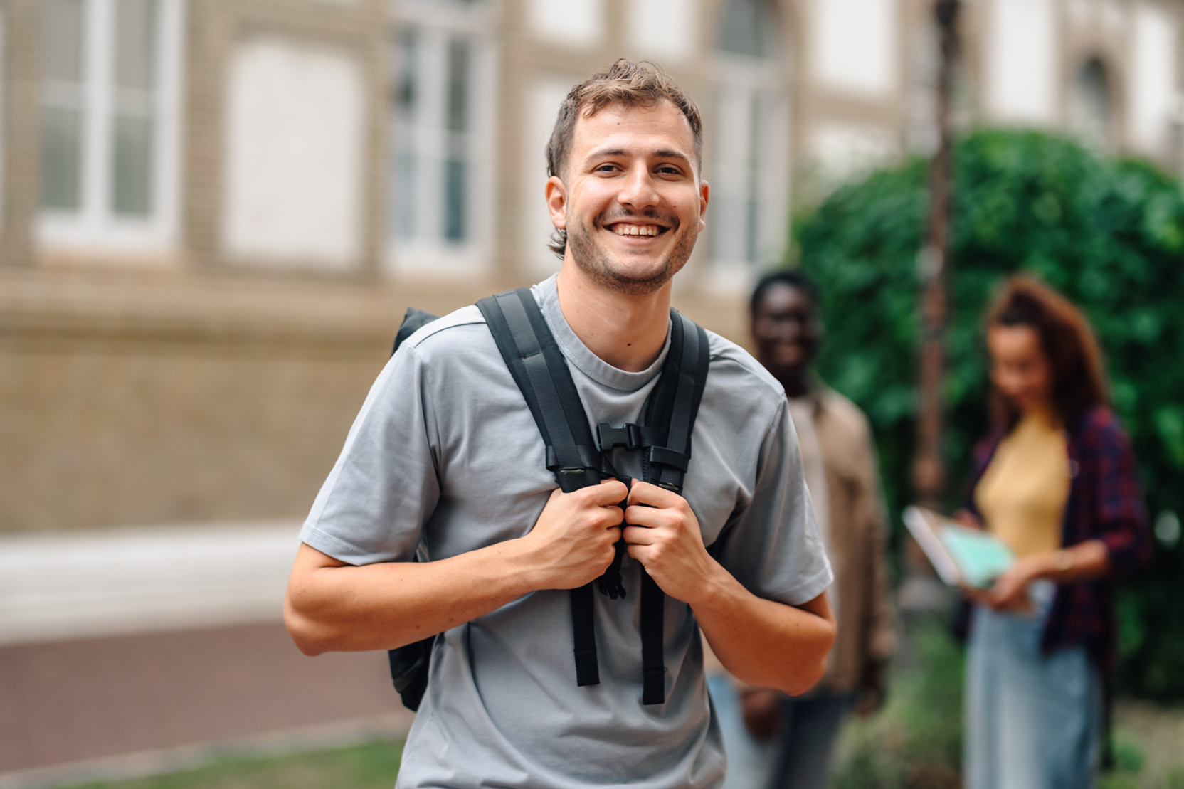 Smiling male student with a backpack on a university campus.