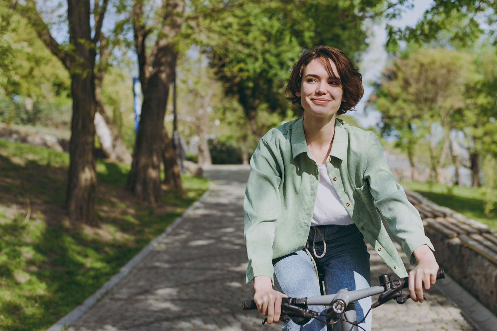 Young woman riding a bicycle along a sunny tree-lined path.