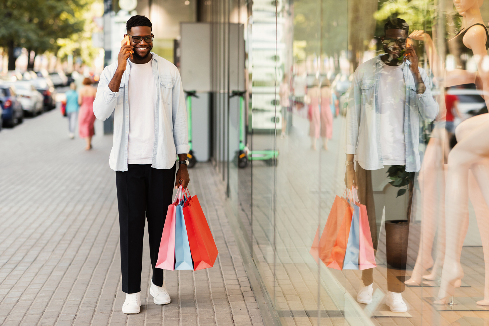 Person carrying shopping bags and talking on the phone while walking along a retail street
