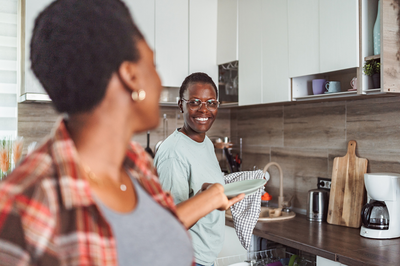 Two roommates smiling and doing dishes together in a bright, modern kitchen.