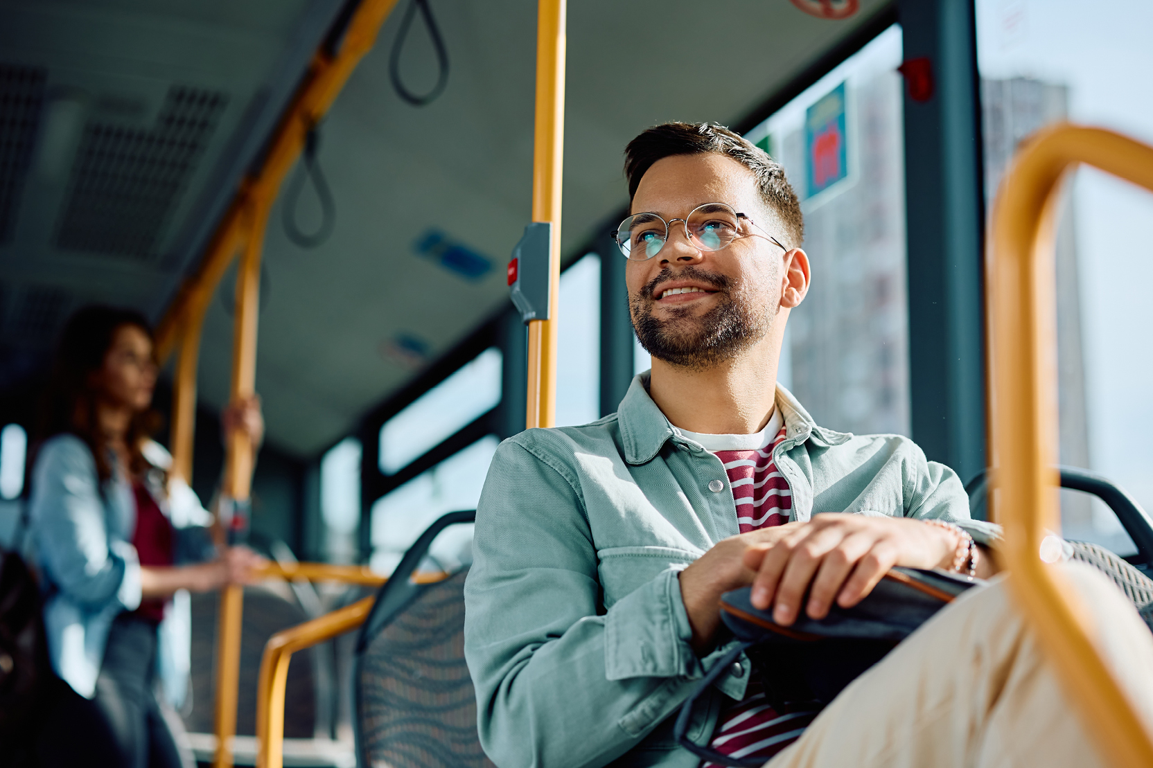 A smiling man rides public transit on a bright, sunny day.