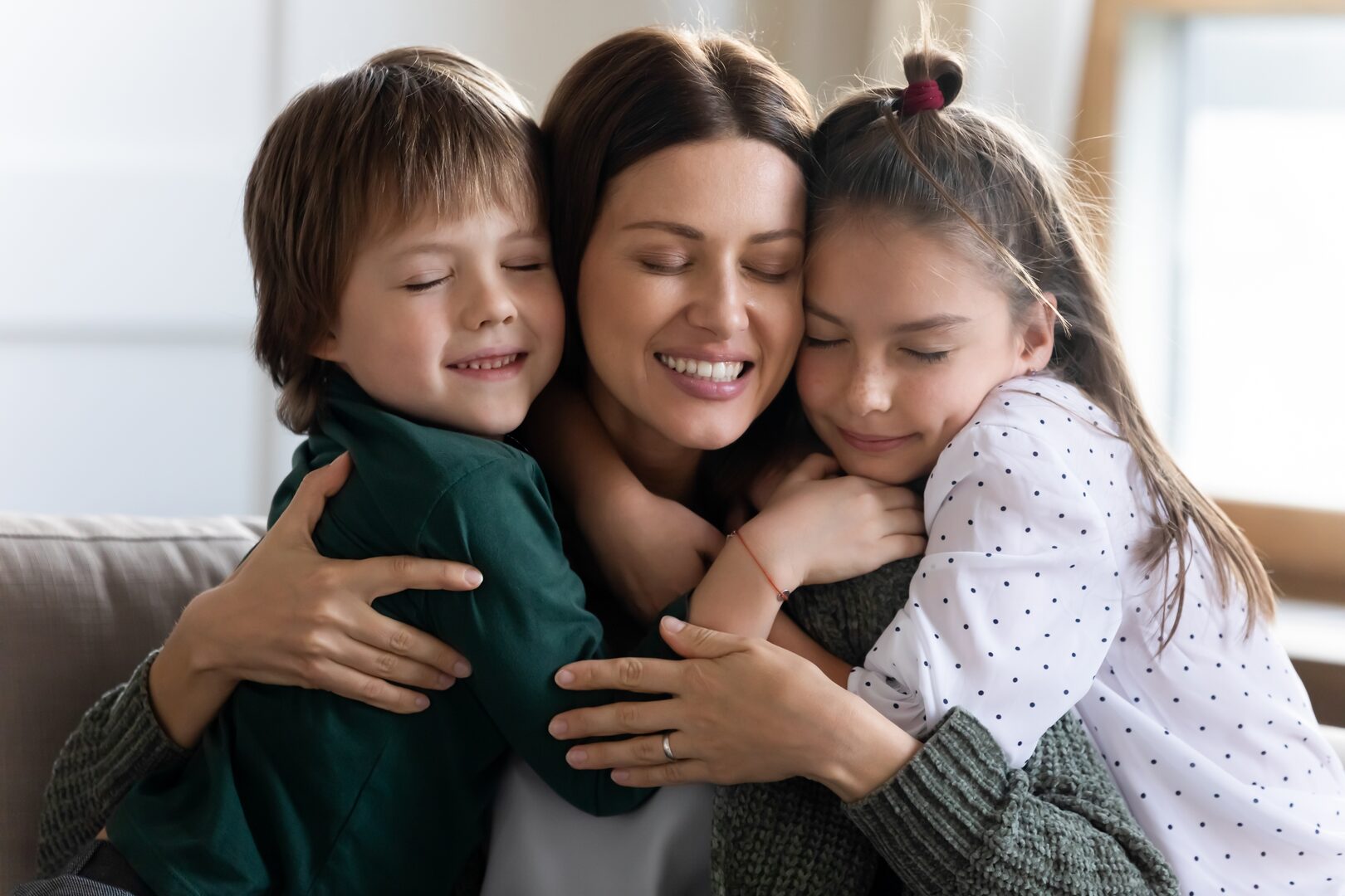 Happy mother hugging two young children on a couch at home