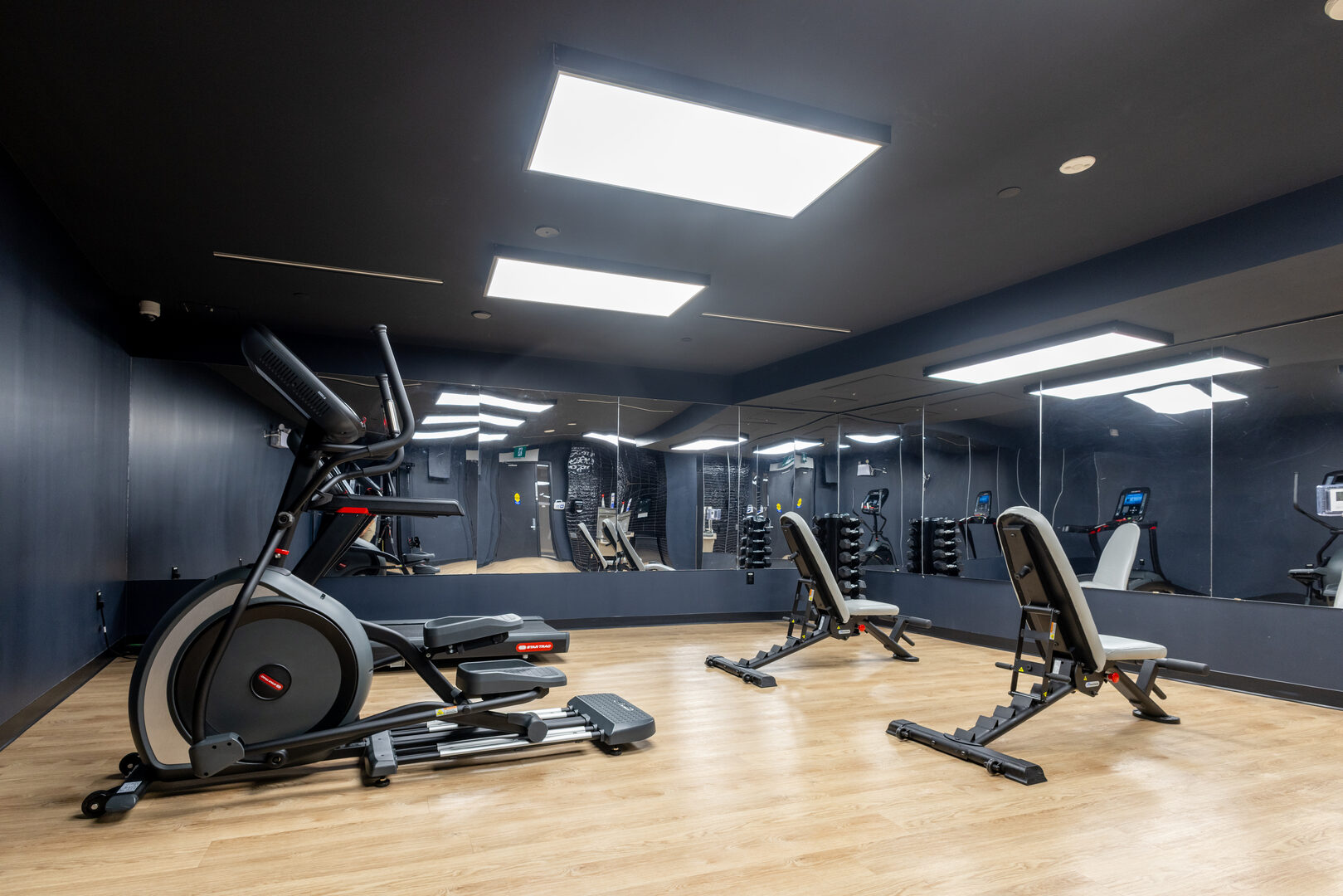 Modern apartment building fitness room with elliptical, weight benches, and mirrored walls