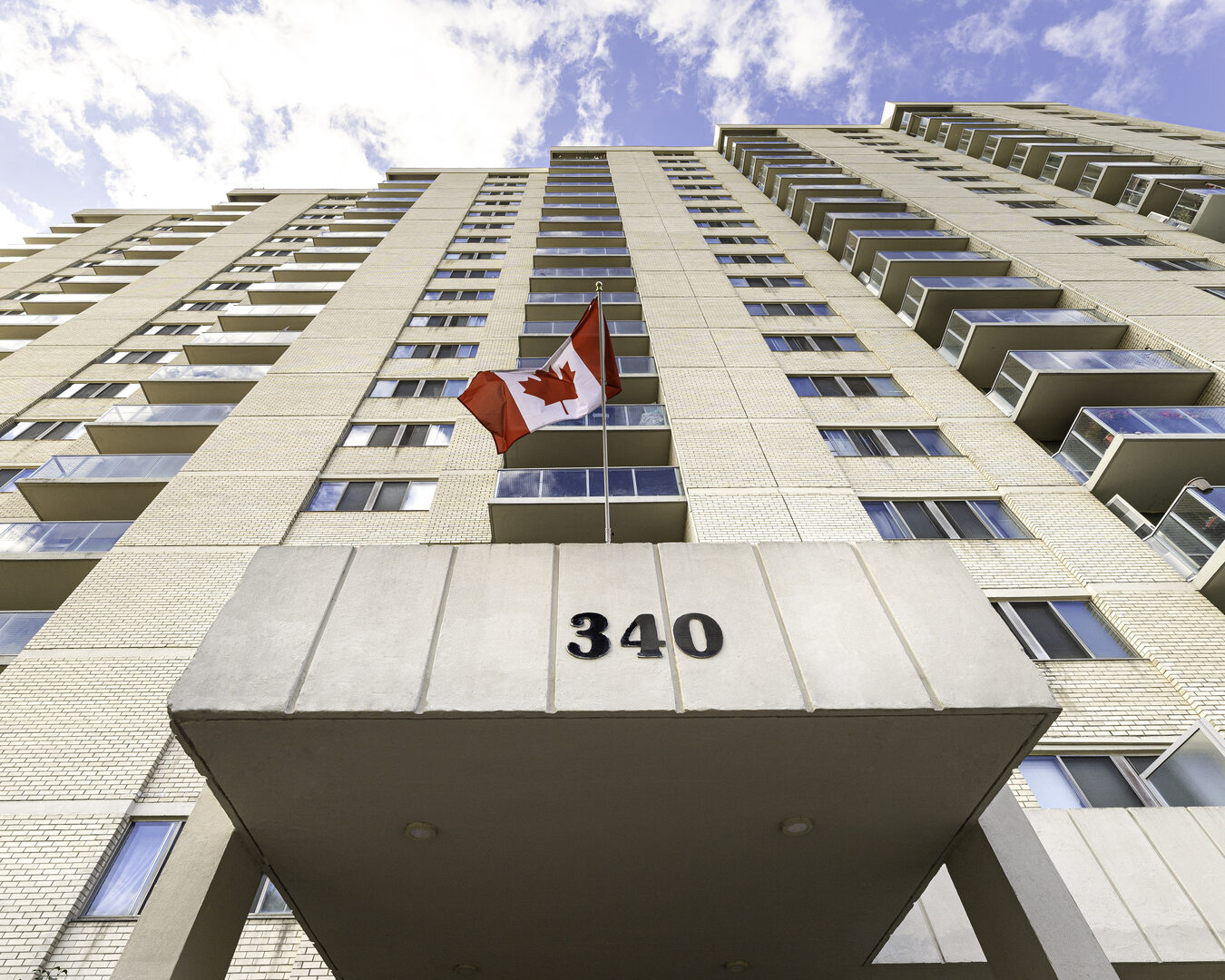 Low-angle view of a Canadian rental apartment building entrance with a Canadian flag