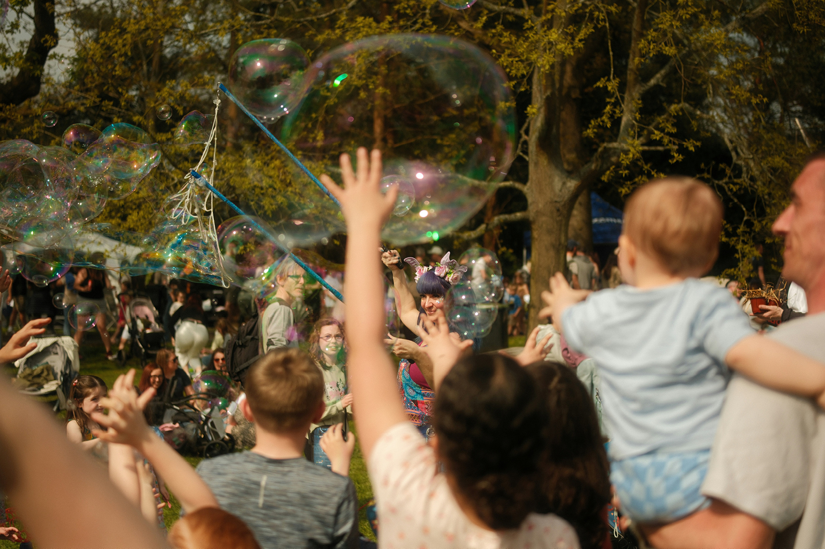 Families reaching for giant soap bubbles at an outdoor festival