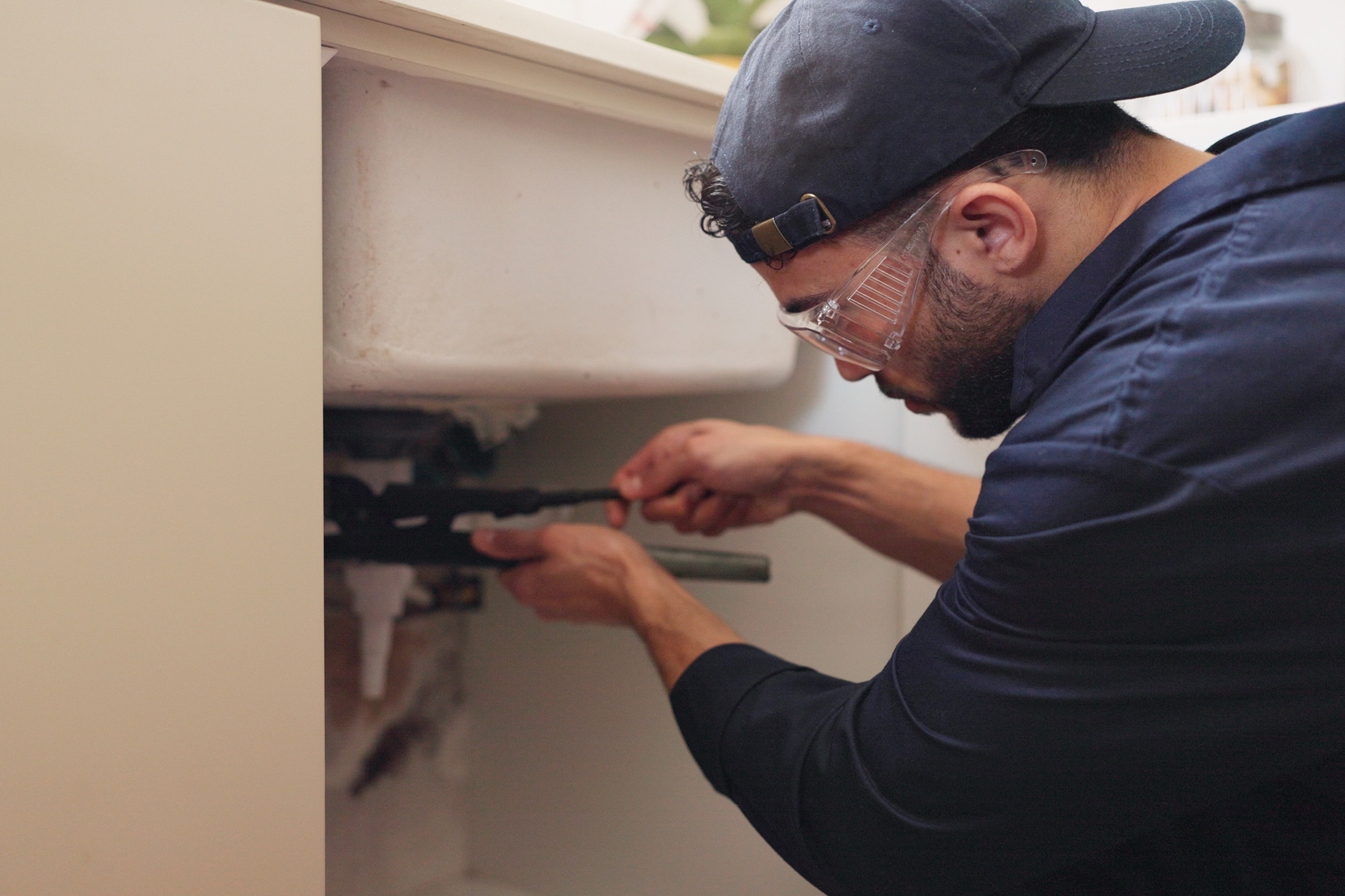 Technician repairing pipes under a sink.