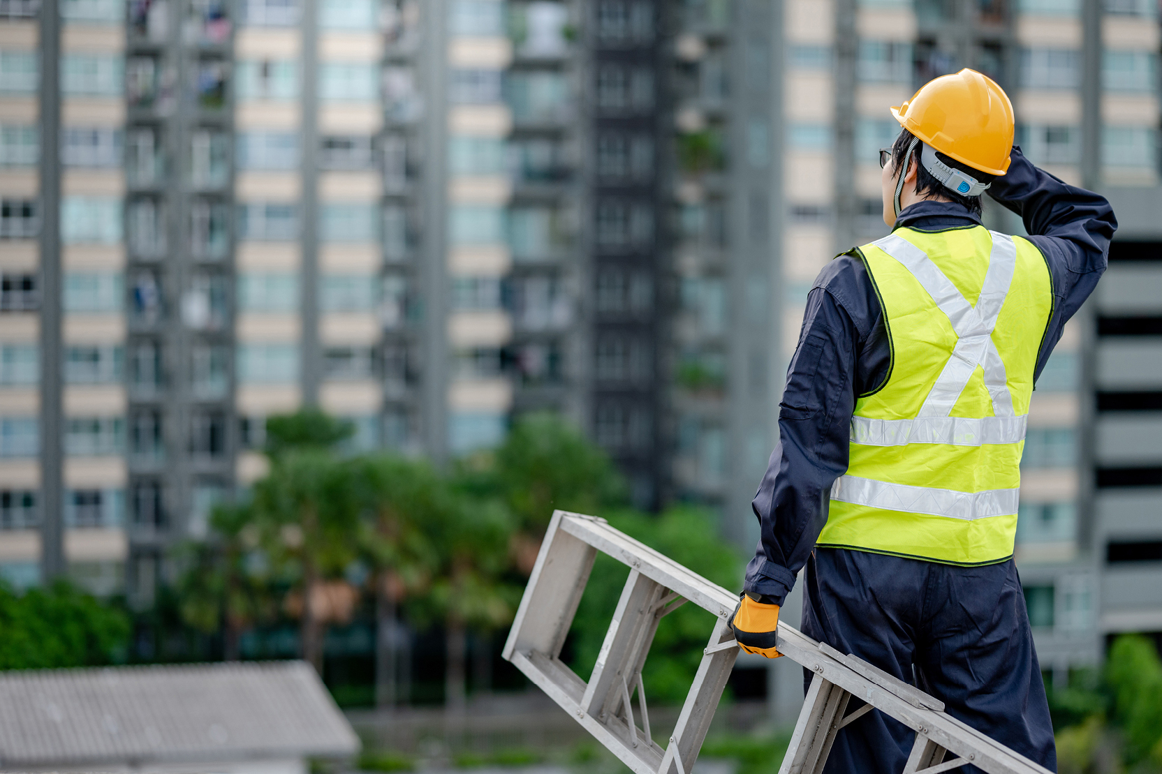 Worker in hard hat holding a ladder near a high-rise.