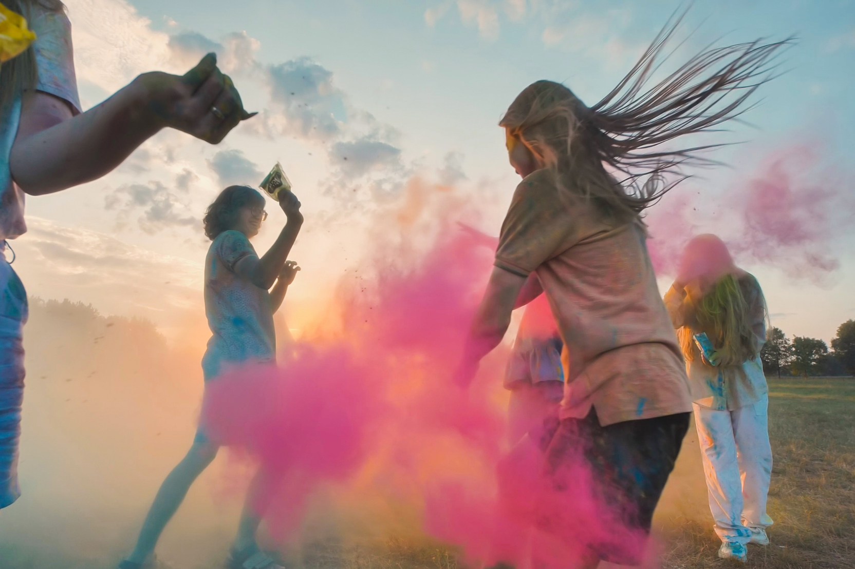 Group of friends throwing colourful powder in a field at sunset.