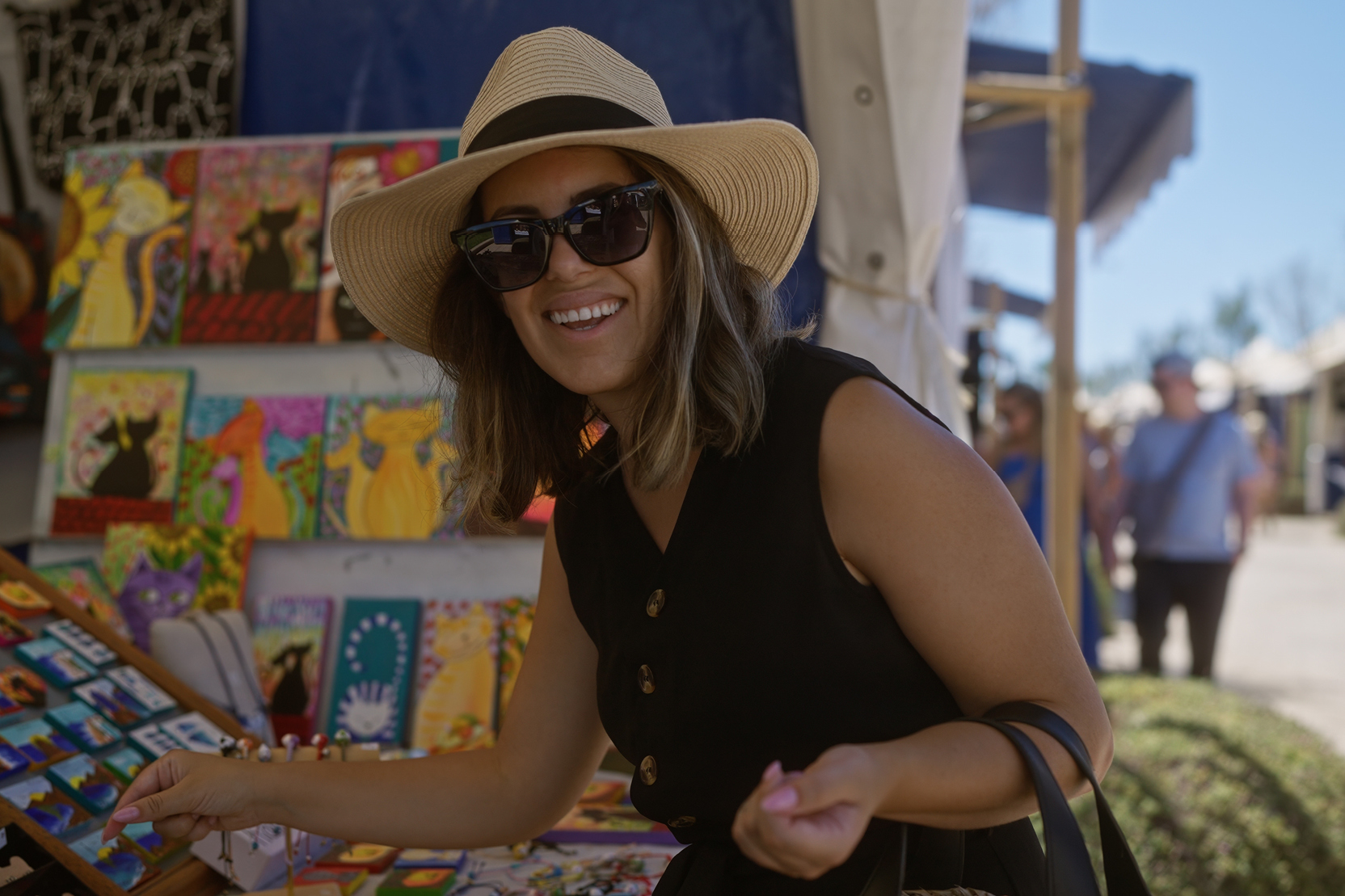 Woman in a sun hat and sunglasses browsing an art market stall.