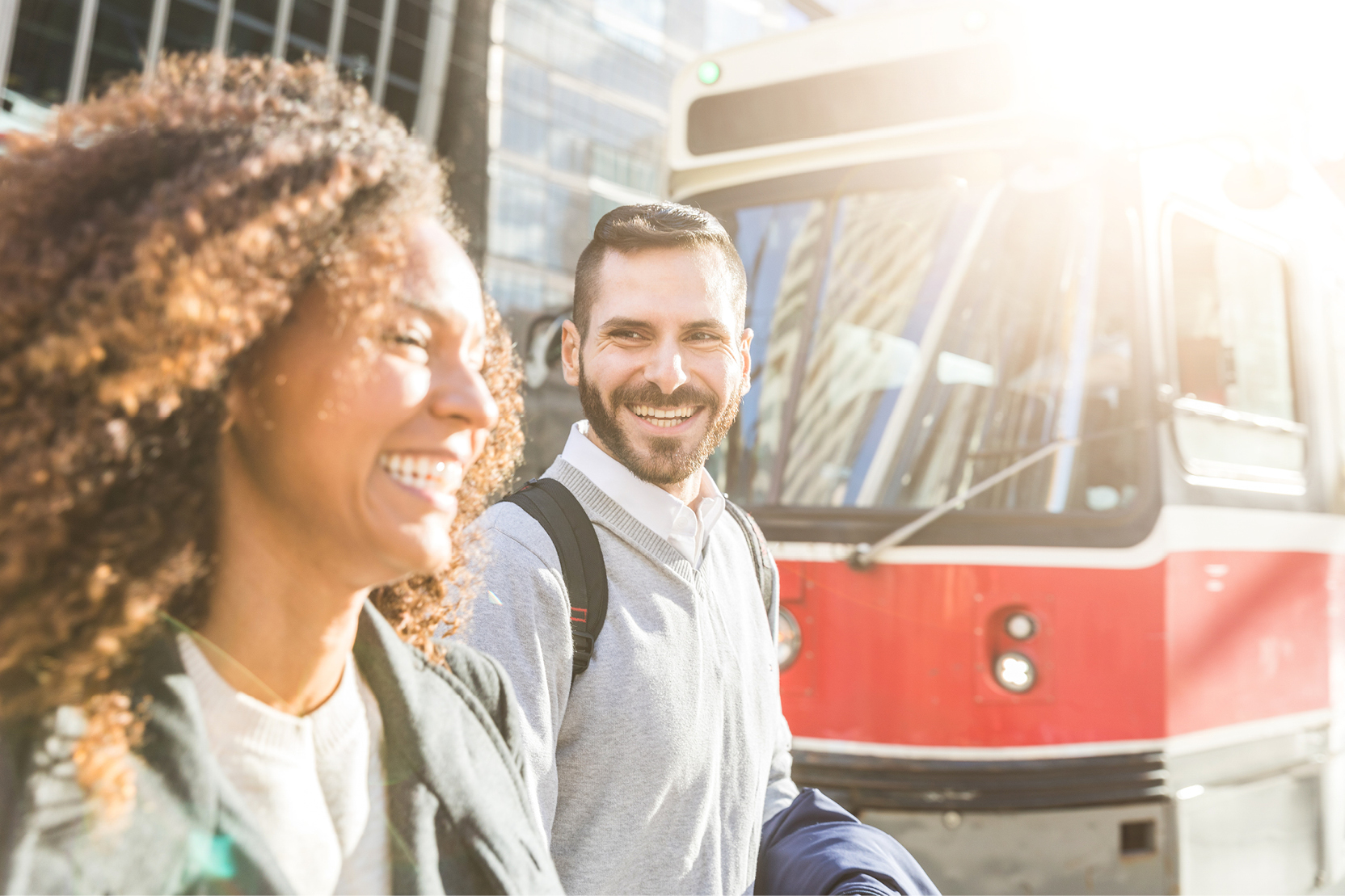A smiling man and woman walking together near a streetcar in the city.