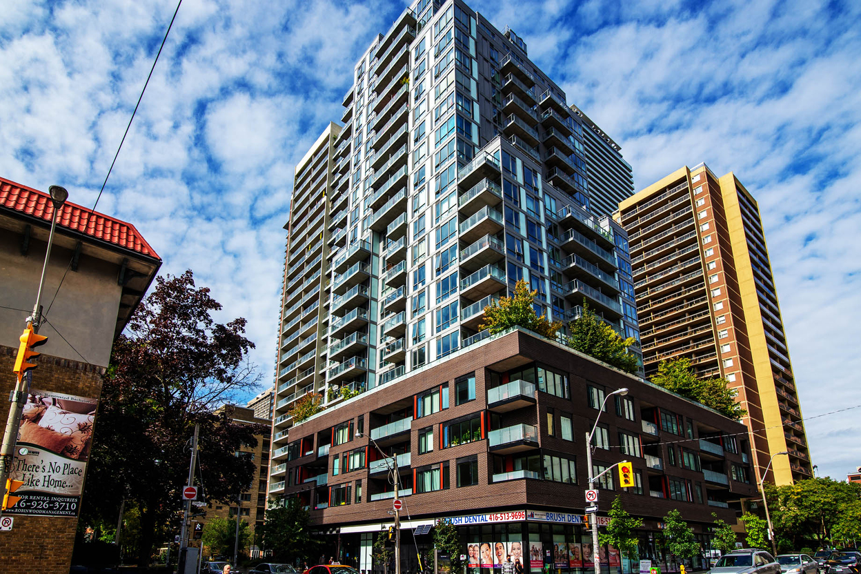 A modern high-rise apartment building with balconies on a city street corner.