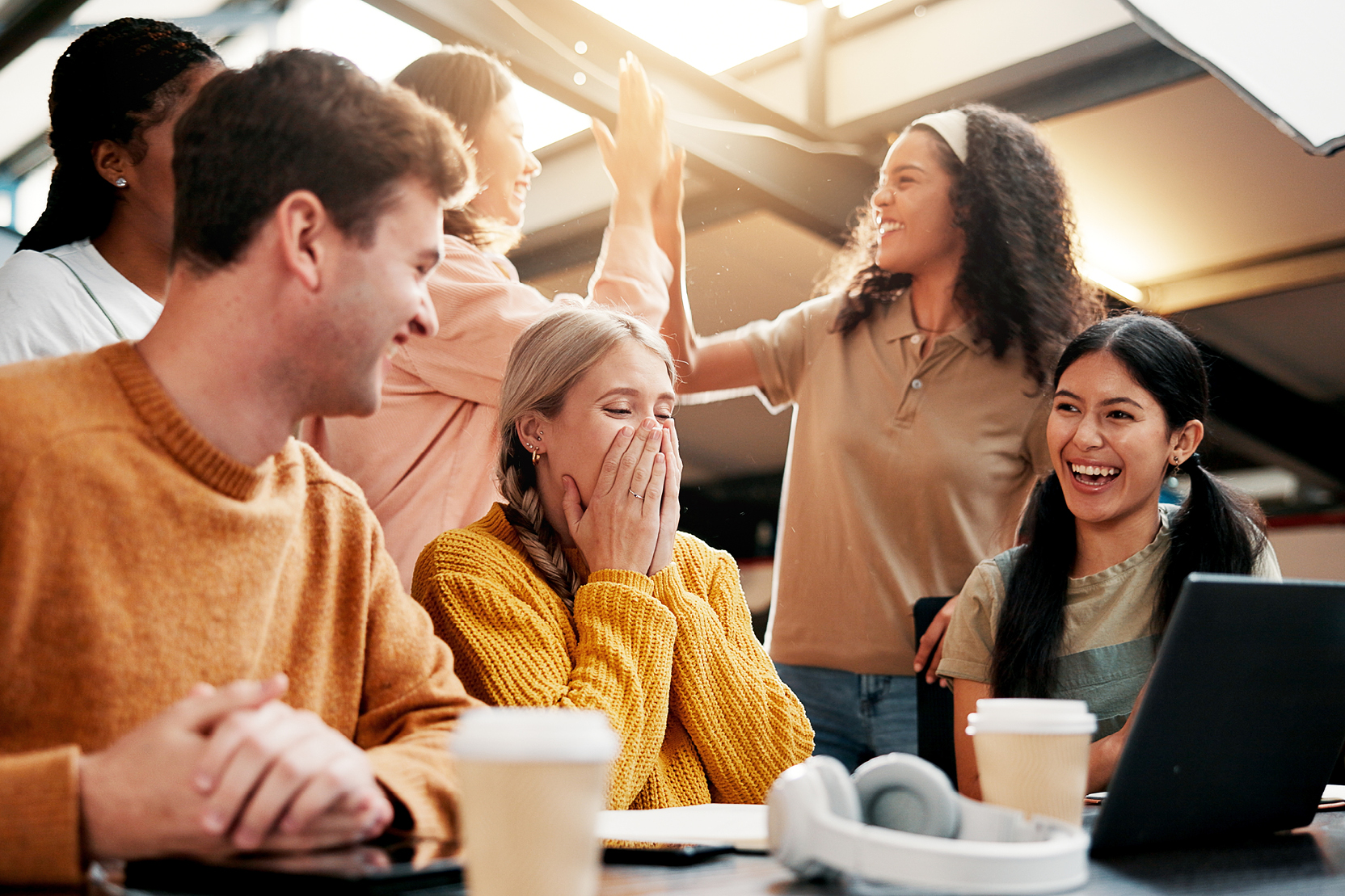 Group of students high-fiving and laughing around a table with coffee and a laptop