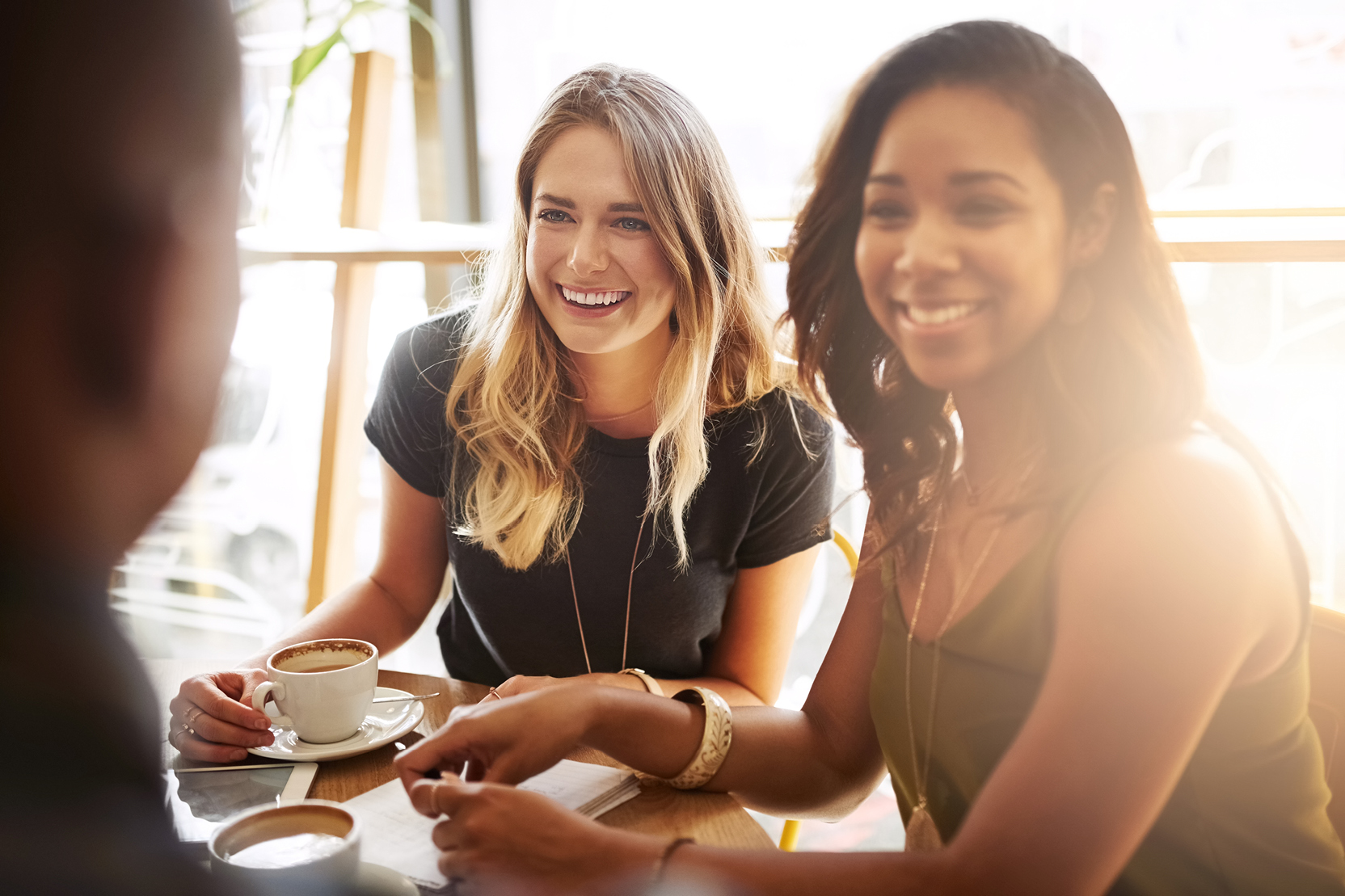 Three friends smiling and chatting over coffee at a café table