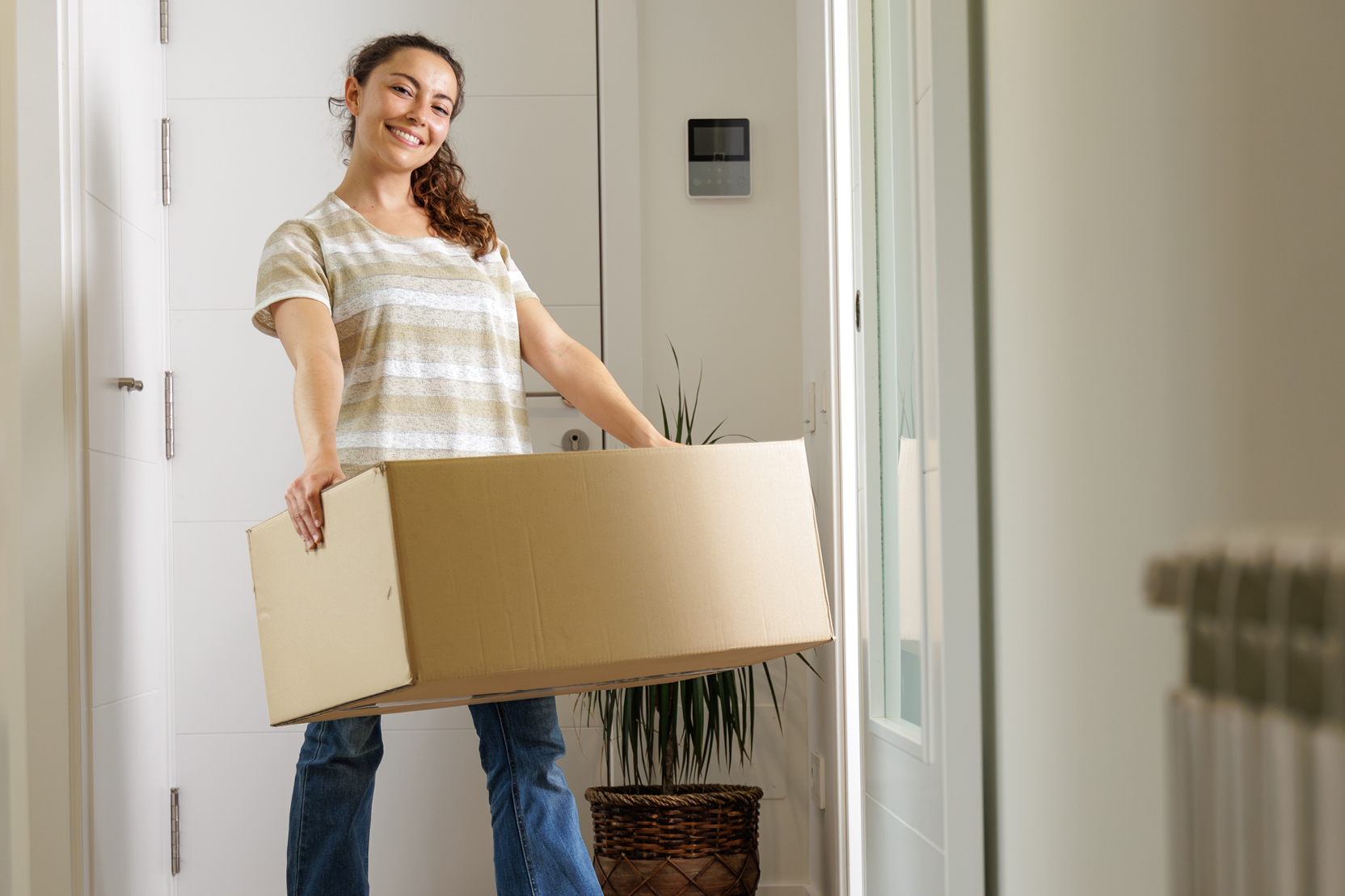 Smiling woman carrying a moving box into her new off-campus apartment