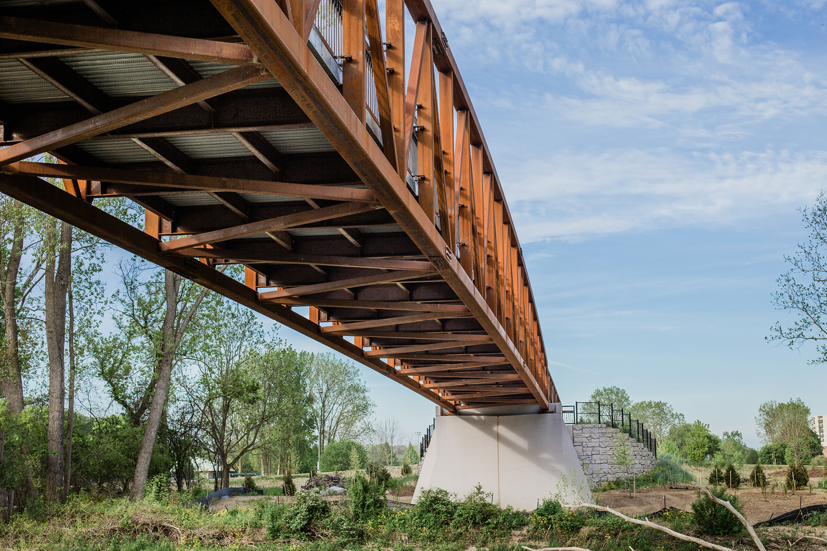 A red-toned bridge spans across the Thames River in London, Ontario.
