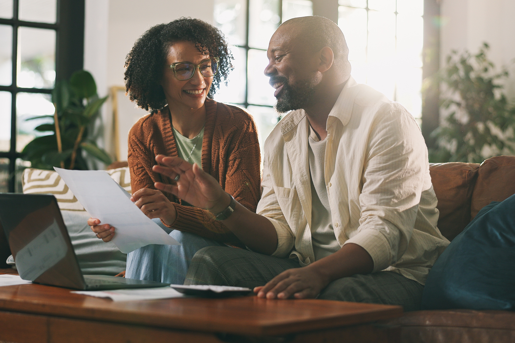 A couple sits in their light-filled living room happily reviewing a document.