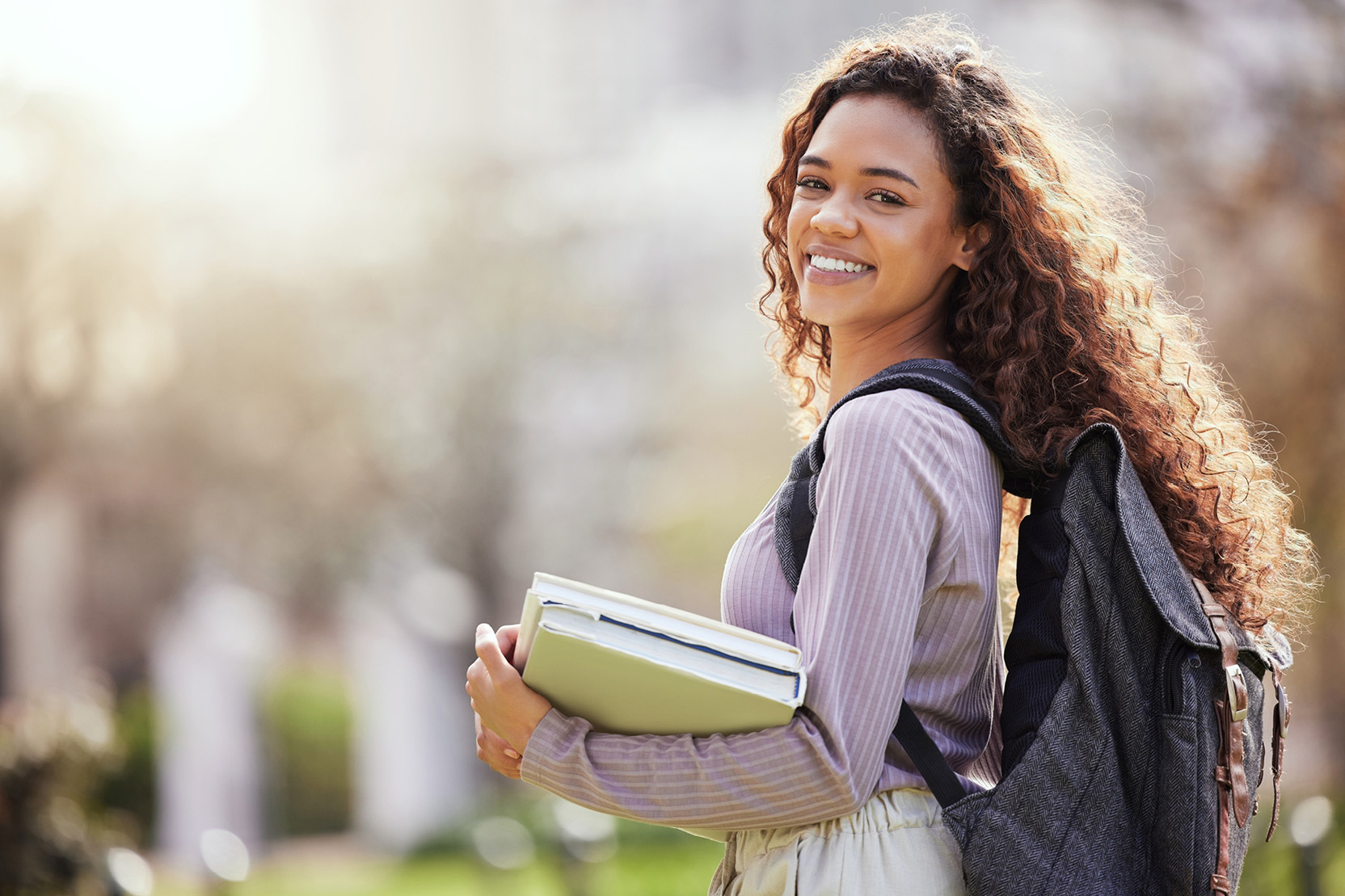 Young woman carries her schoolbooks across campus.