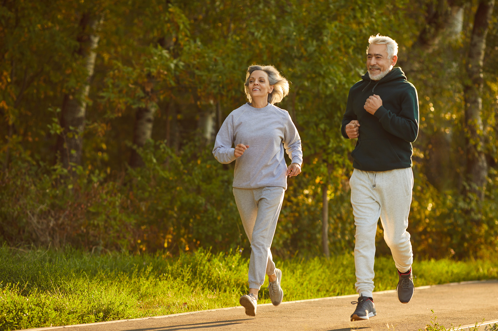 Two joggers in their 60s run on a trail in the sunshine.