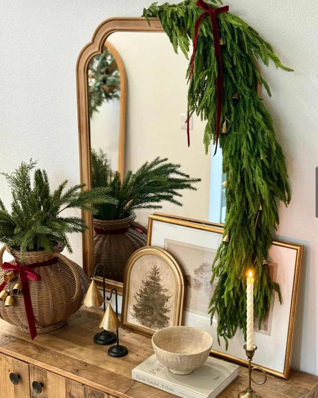 Holiday vignette in a luxury apartment featuring a gold-framed mirror with cascading greenery, paired with candles and vintage-inspired holiday accents.