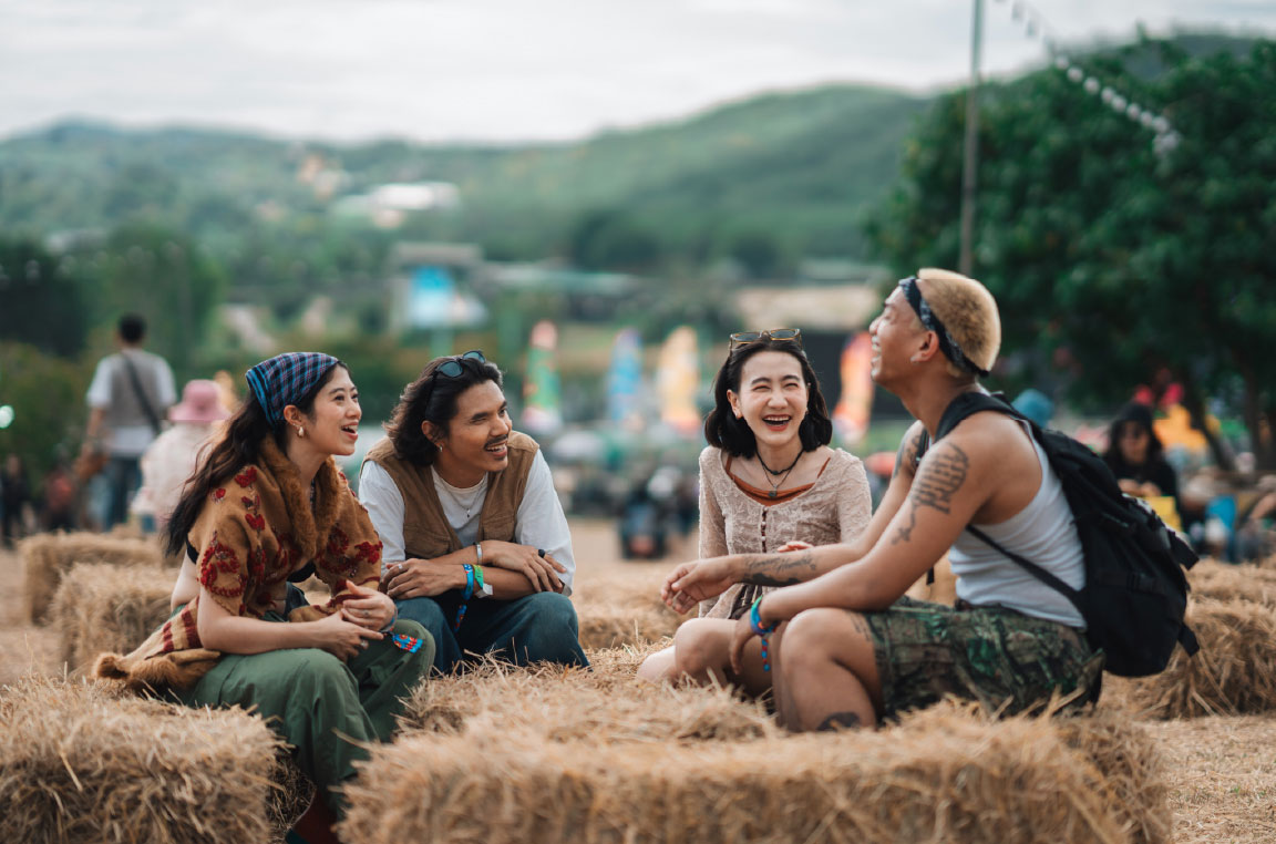 Four friends sitting on hay bales and talking at a festival