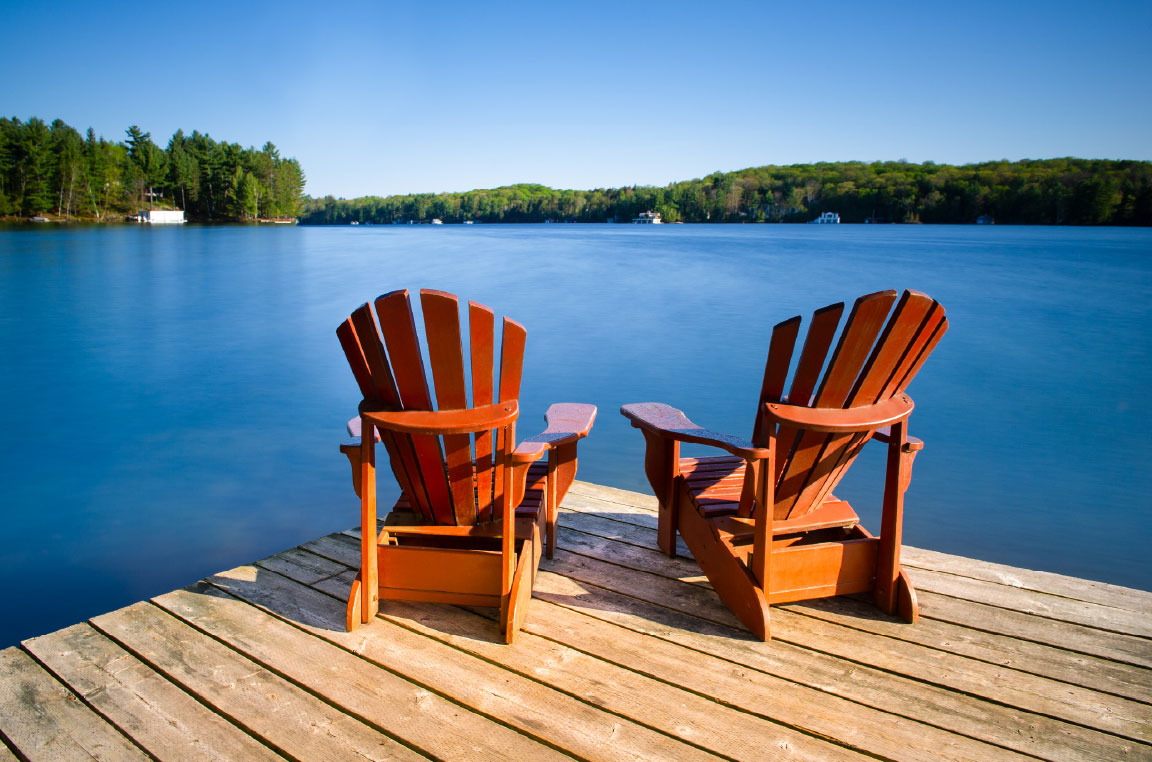 Two wooden chairs facing the waterfront and tree-lined shore