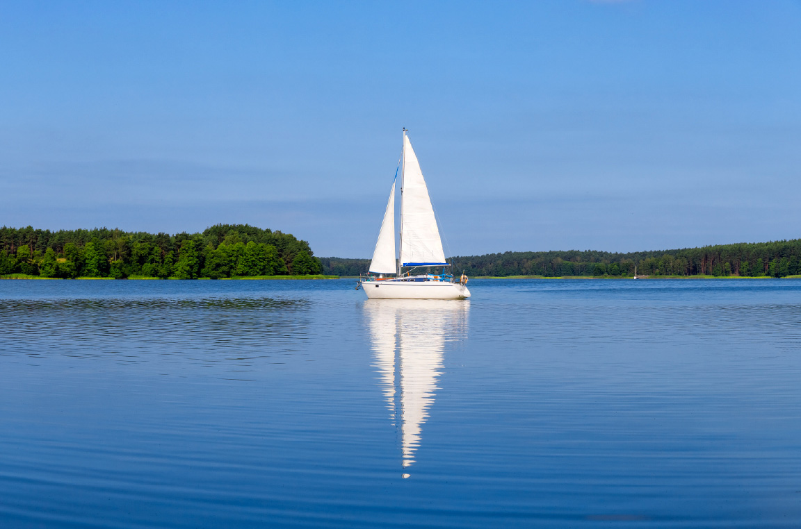 White sailboat sailing along the Sarnia waterfront, with a tree-lined shoreline in the background.