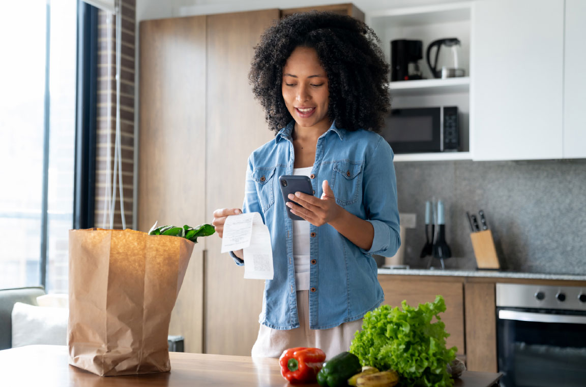 Woman in her apartment checking her grocery bill after purchasing groceries.