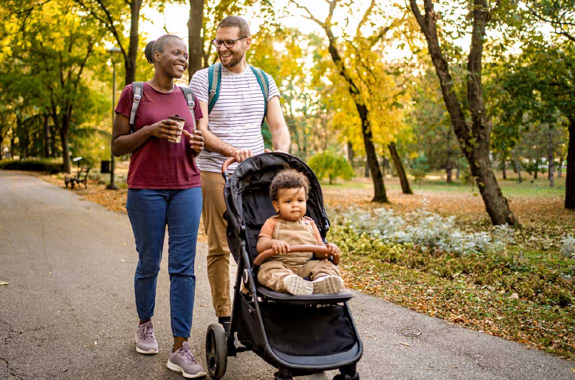 Young family walking together on a tree-lined path with their baby in a stroller
